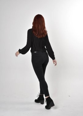 Siyah kot pantolon, bot ve bluz giyen kızıl saçlı güzel bir kızın portresi. Stüdyonun arka planında tam boy poz, kamera arkası....