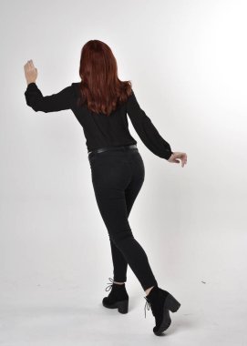 Siyah kot pantolon, bot ve bluz giyen kızıl saçlı güzel bir kızın portresi. Stüdyonun arka planında tam boy poz, kamera arkası....