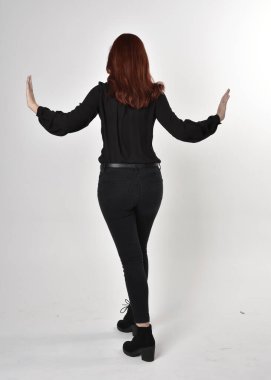 Siyah kot pantolon, bot ve bluz giyen kızıl saçlı güzel bir kızın portresi. Stüdyonun arka planında tam boy poz, kamera arkası....