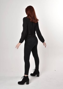 Siyah kot pantolon, bot ve bluz giyen kızıl saçlı güzel bir kızın portresi. Stüdyonun arka planında tam boy poz, kamera arkası....