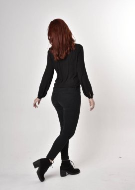 Siyah kot pantolon, bot ve bluz giyen kızıl saçlı güzel bir kızın portresi. Stüdyonun arka planında tam boy poz, kamera arkası....