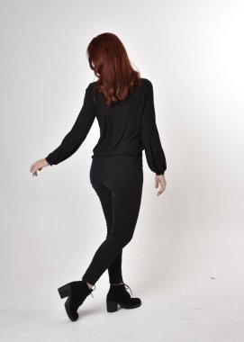 Siyah kot pantolon, bot ve bluz giyen kızıl saçlı güzel bir kızın portresi. Stüdyonun arka planında tam boy poz, kamera arkası....