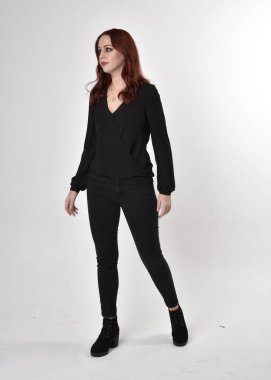 Siyah kot pantolon, bot ve bluz giyen kızıl saçlı güzel bir kızın portresi. Stüdyonun arka planında, kameraya doğru dik bir poz..