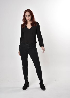 Siyah kot pantolon, bot ve bluz giyen kızıl saçlı güzel bir kızın portresi. Stüdyonun arka planında, kameraya doğru dik bir poz..