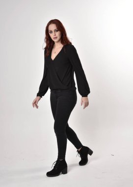 Siyah kot pantolon, bot ve bluz giyen kızıl saçlı güzel bir kızın portresi. Stüdyonun arka planında, kameraya doğru dik bir poz..