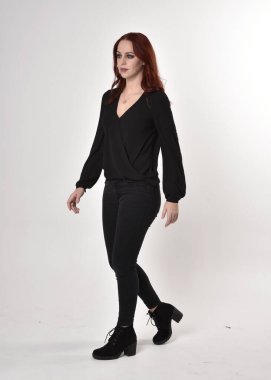 Siyah kot pantolon, bot ve bluz giyen kızıl saçlı güzel bir kızın portresi. Stüdyonun arka planında, kameraya doğru dik bir poz..