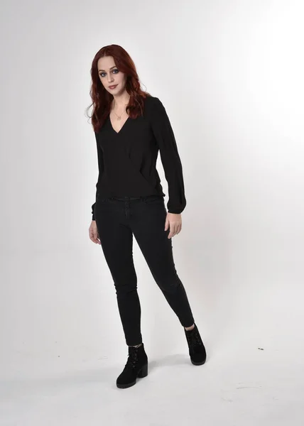 一个红头发 穿着黑色牛仔裤 靴子和衬衫的漂亮女孩的画像 全长站立姿势 面对着相机 在工作室的背景下 — 图库照片