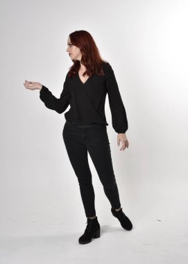 Siyah kot pantolon, bot ve bluz giyen kızıl saçlı güzel bir kızın portresi. Stüdyonun arka planında el hareketleriyle kameraya doğru uzun bir duruş..