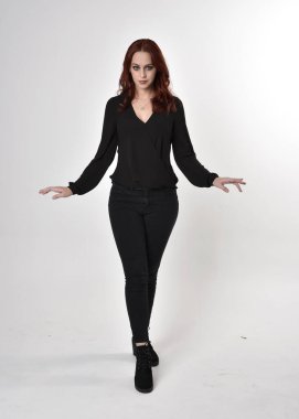 Siyah kot pantolon, bot ve bluz giyen kızıl saçlı güzel bir kızın portresi. Stüdyonun arka planında el hareketleriyle kameraya doğru uzun bir duruş..