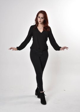 Siyah kot pantolon, bot ve bluz giyen kızıl saçlı güzel bir kızın portresi. Stüdyonun arka planında el hareketleriyle kameraya doğru uzun bir duruş..
