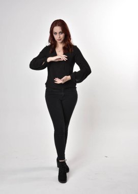 Siyah kot pantolon, bot ve bluz giyen kızıl saçlı güzel bir kızın portresi. Stüdyonun arka planında el hareketleriyle kameraya doğru uzun bir duruş..