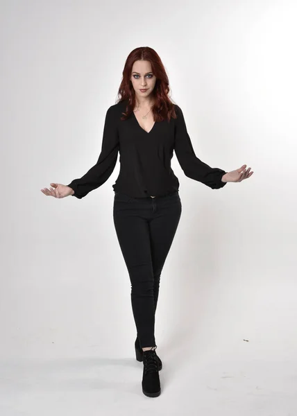 一个红头发 穿着黑色牛仔裤 靴子和衬衫的漂亮女孩的画像 全长站立姿势 在工作室背景上以手势面对镜头 — 图库照片