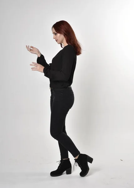 一个红头发 穿着黑色牛仔裤 靴子和衬衫的漂亮女孩的画像 全长站立姿势 在工作室背景上 — 图库照片