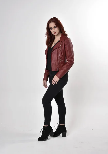 黒のジーンズと革のジャケットとブーツを身に着けている赤い髪のきれいな女の子の肖像画 スタジオの背景に立つ長さのポーズ — ストック写真