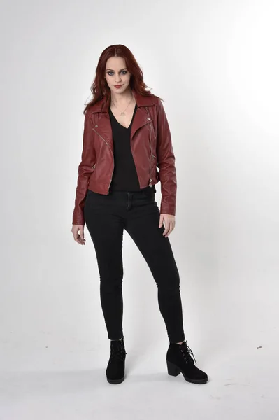 一个红头发的漂亮女孩穿着黑色牛仔裤和皮夹克靴子的画像 全长站立姿势在工作室的背景上 — 图库照片