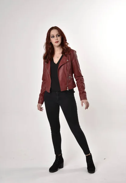 黒のジーンズと革のジャケットとブーツを身に着けている赤い髪のきれいな女の子の肖像画 スタジオの背景に立つ長さのポーズ — ストック写真