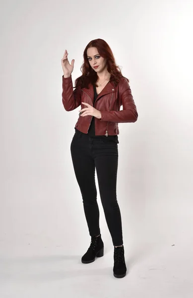 一个红头发的漂亮女孩穿着黑色牛仔裤和皮夹克靴子的画像 在演播室的背景上以手势站得整整齐齐 — 图库照片