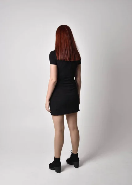 短い黒のドレスとブーツを身に着けている赤い髪を持つ可愛い女の子の肖像画 スタジオの背景に完全な長さ立ってポーズ — ストック写真