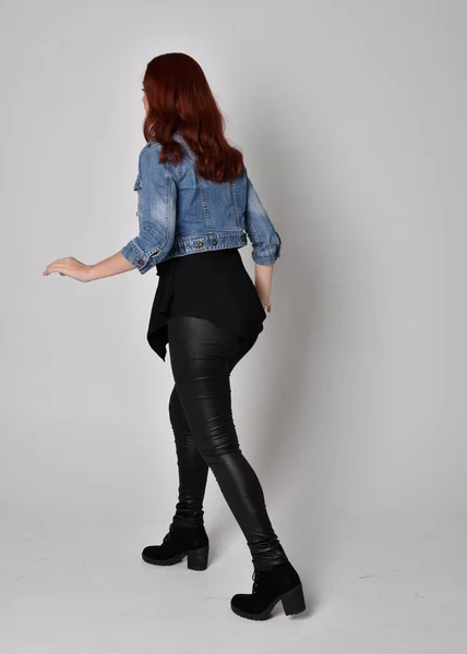 一个红头发 穿着黑色皮裤和牛仔夹克的漂亮姑娘的肖像 全长站立姿势 与灰色工作室背景隔离 — 图库照片