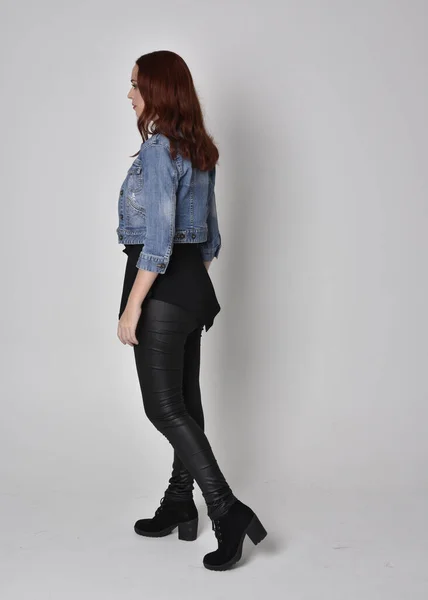 一个红头发 穿着黑色皮裤和牛仔夹克的漂亮姑娘的肖像 全长站立姿势 与灰色工作室背景隔离 — 图库照片