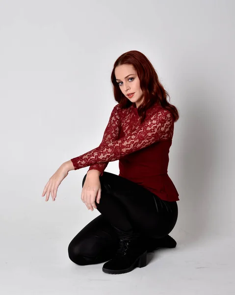 一个穿着皮裤和长袖花边衬衫的红头发美女的画像 与工作室背景隔离的全长屈膝姿势 — 图库照片