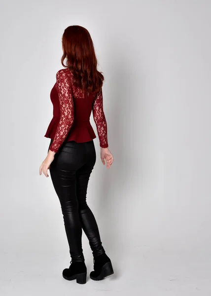 一个穿着皮裤和长袖花边衬衫的红头发美女的画像 全长站立姿势 面对着相机 与工作室背景隔离 — 图库照片