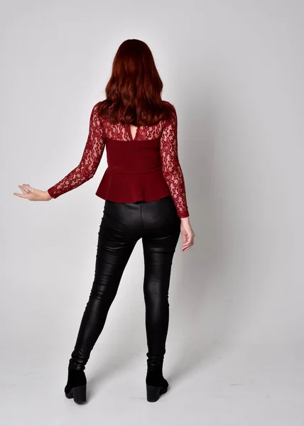 一个穿着皮裤和长袖花边衬衫的红头发美女的画像 全长站立姿势 面对着相机 与工作室背景隔离 — 图库照片