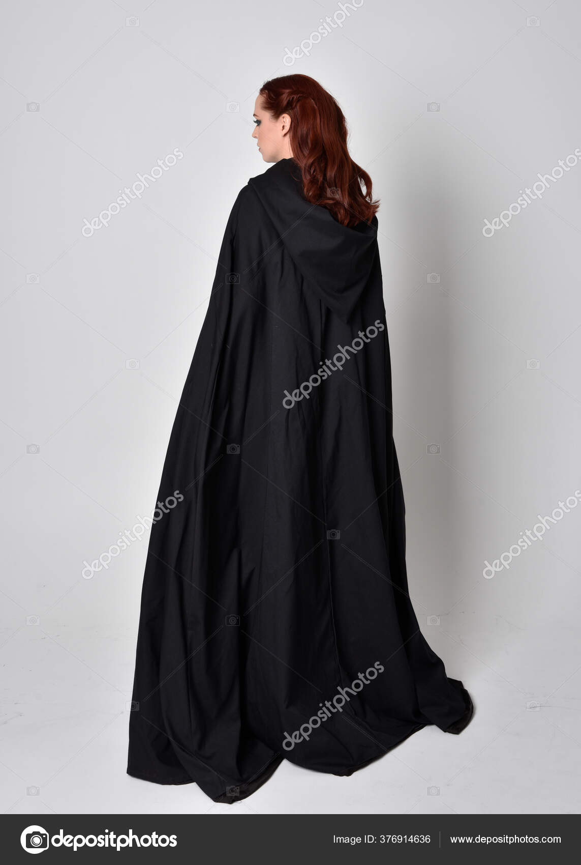 一个穿着黑色长斗篷的女人的幻想画像全长站立姿势背对着相机与工作室背景隔离 图库照片 C Faestock