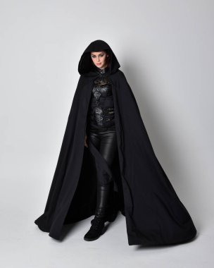 fantasy portrait of a woman with red hair wearing dark leather assassin costume with long black cloak. Full length standing pose  isolated against a studio background. clipart