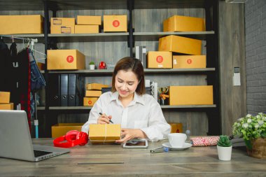 İş kadını ürünleri ve siparişleri tabletle birlikte kontrol ediyor, karton kutu paketleme, başlangıç ve küçük işletmelerle online satış, ev ve internet üzerinden ticaret sektörü ile konsept işi