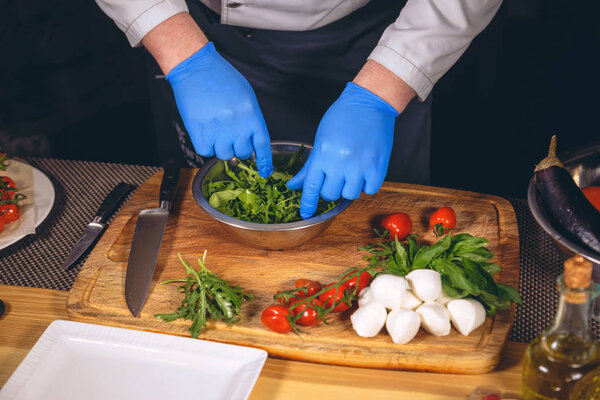 Chef hands with gloves cooked. Chef  is cooking a  gourmet dish - mozzarella with basil, cherry tomatoes and arugula. 