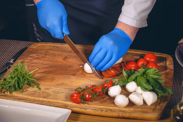 Şef eller eldiven ile pişirilir. Şef bir gurme yemek - mozzarella fesleğen, domates ve roka ile pişirme. 