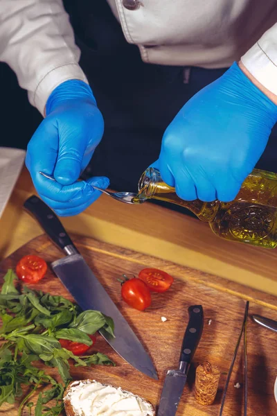 Şef eller eldiven ile pişirilir. Şef bir gurme yemek - mozzarella fesleğen, domates ve roka ile yemek pişiriyor. Şef zeytinyağı dökülür
