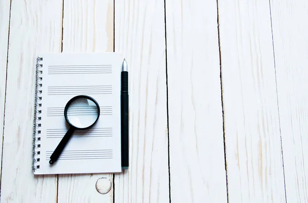 Lupa, cuaderno, bolígrafo sobre fondo de madera blanca — Foto de Stock