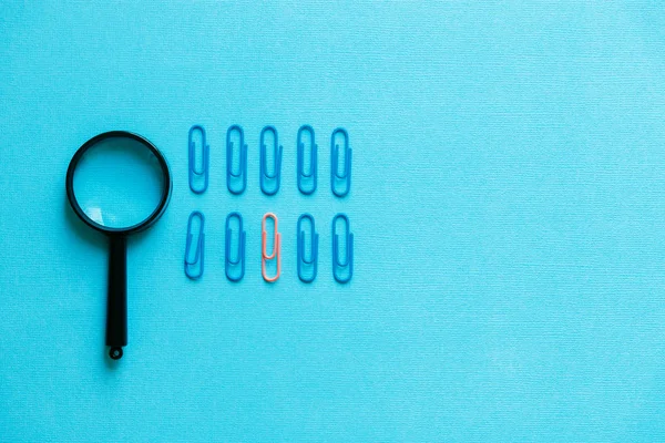 Uma lupa e clipes de papel sobre um fundo azul — Fotografia de Stock