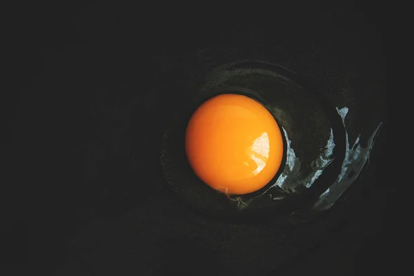 raw egg with yellow egg broken into a frying pan