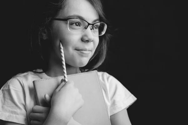 pretty cute smiling girl in glasses white t-shirt with copybook pencil on black background. black and white image