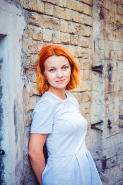 sevimli ateşli Kızıl saçlı gri-mavi gözlü kız tuğla duvar tarafından ayakta