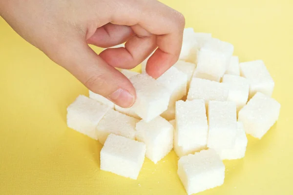 Main d'enfant prend le sucre raffiné blanc dispersé au hasard sur fond jaune — Photo