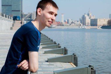 mavi gömlekli adam duran, nehrin sahildeki korkuluk üzerine eğilerek ve parlak güneş'ten şaşı