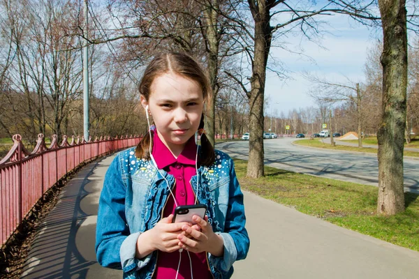 girl in warm sunny weather on the street with headphones listening to music in the gadget