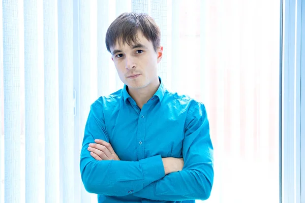 Retrato de um jovem bonito homem em uma camisa azul perto da janela — Fotografia de Stock