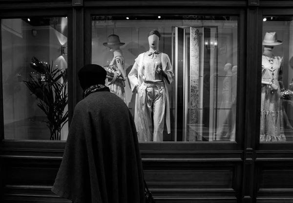 बुजुर्ग महिला महंगे कपड़े की दुकान की खिड़की से गुजर रही काले और सफेद तस्वीर — स्टॉक फ़ोटो, इमेज
