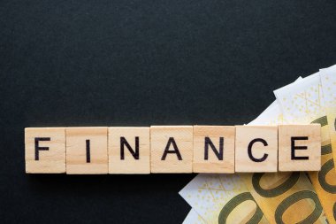 Finans sözcükleri ve para banknotları koyu arkaplanda tahta küplerle çapraz bulmacada toplanır.