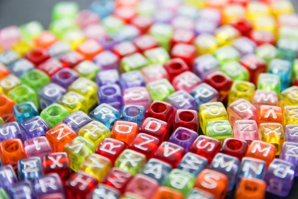 A bunch of little multicolored letters on the surface of a dark background, selective focus — Stock Photo, Image