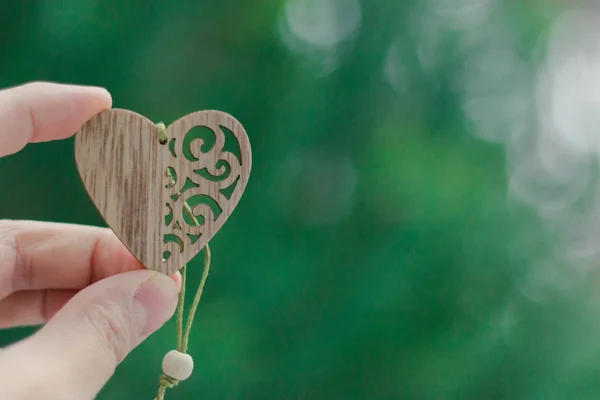 Luminoso sfondo festivo, San Valentino, amore piccolo cuore di legno nella mano delle donne su sfondo verde — Foto Stock