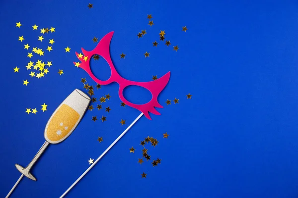 Party time, fun, flatlay overhead black paper photo stand props stars champagne glass mask blue background copy space