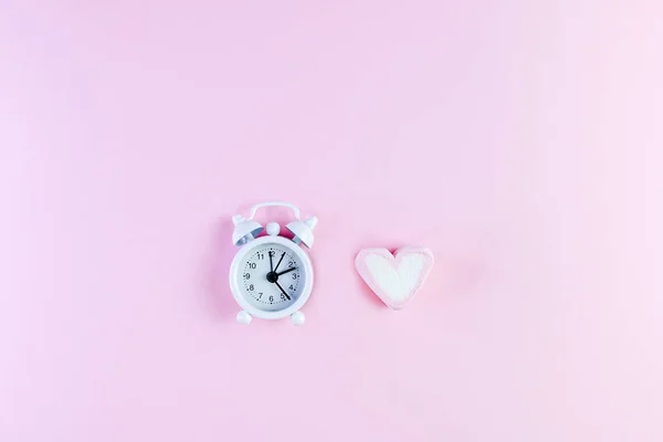 Pastel Valentine achtergrond is gemaakt van marshmallow souffle in de vorm van hartjes op een roze achtergrond en een klok. Valentijnsdag concept met kopieerruimte, tijd om lief te hebben — Stockfoto