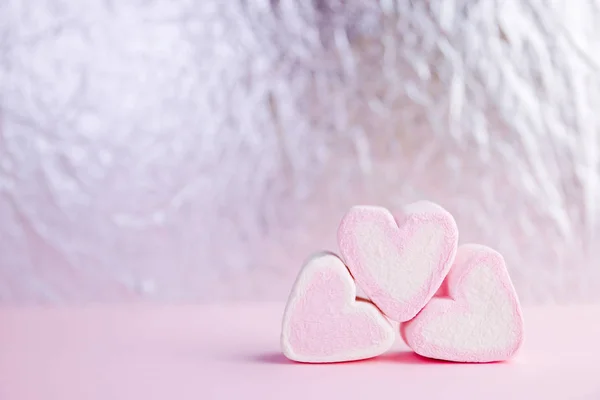Pastel valentine background made of marshmallows souffle in the form of hearts on a pink and silver background. Valentine\'s Day concept with copy space