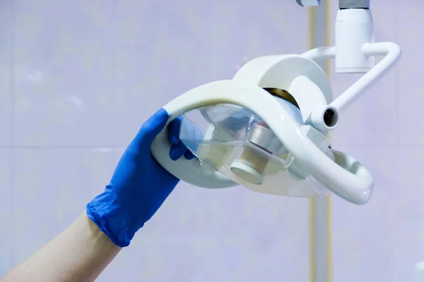 Biuro dentystyczne. Ręka doktora trzyma bezcieniową lampę nad fotelem dentystycznym. Wyposażenie gabinetu stomatologicznego — Zdjęcie stockowe